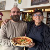 Der neue Inhaber Claudiu Craciun der Pizzeria Pronto Salvatore steht gemeinsam mit dem ehemaligen Besitzer Salvatore Grasso vor der Verkaufstheke im Restaurant. Sie halten gemeinsam einen Teller mit einer neapolitanischen Pizza in der Hand.