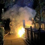 Ein Feuerwehrmann steht vor brennenden Mülltonnen.