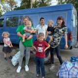 Eine Familie mit Kindern steht in der Ukraine vor einem blauen Lieferwagen