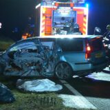 Das zerstörte Auto steht frontal an einer Leitplanke. Dahinter sind Rettungswagen und Rettungskräfte zu sehen.