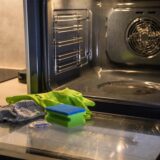 Vor einem geöffneten Backofen liegen ein Schwamm, Handschuhe und ein Spülmaschinen-Tab.
