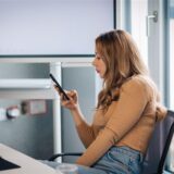 Eine Frau sitzt im Büro und hat ein Handy in der Hand.