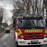 Ein Einsatzwagen der Feuerwehr steht auf einer Straße vor dem Wertstoffhof in Holzwickede. Im Hintergund ist ein Container zu sehen.
