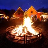 Ein Lagerfeuer sorgt im Dunkeln für ein besonderes Flair auf dem Weihnachtsmarkt auf Gut Keinemann in Rünthe. Im Hintergrund sind beleuchtete Häuser und Buden zu sehen.