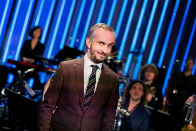 Jan Böhmermann steht im Anzug vor dem Rundfunk Tanzorchester Ehrenfeld.