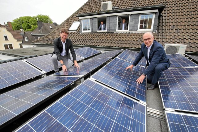 Unnas Stadtwerkechef Jürgen Schäpermeier und Matthias Fischer von der UKBS stehen auf einem Dach zwischen Solarstromanlagen.