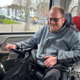 Kai Gungl sitzt im Rollstuhl in einer Stadtbahn mit seinem Assistenzhund Bella (12).
