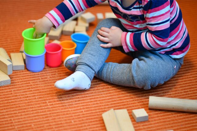 Ein Mädchen spielt in einer Kita mit bunten Bechern und Bauklötzen.