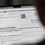 Auf einem Computerbildschirm ist der Ausschnitt eines Antrags auf Kindergeld zu sehen. Im Vordergrund erscheint am rechten Bildrand die unscharfe, dunkle Form einer Person, die auf den Bildschirm schaut. Von der Person sind der halbe Kopf und der Hals zu sehen.