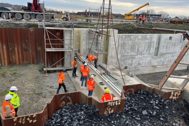 Bauarbeiter setzen am Adensee in Bergkamen ein Verschlussbauwerk ein.