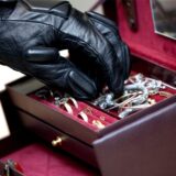 Eine Hand mit schwarzem Handschuh greift in eine dunkelrote Schmuckschatulle und greift sich Schmuck.