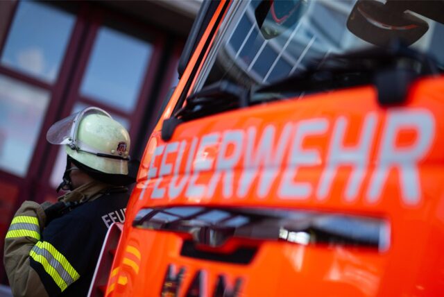Ein Feuerwehrmann, der arbeitet im Hintergrund. Im Vordergrund ein Feuerwehrwagen.