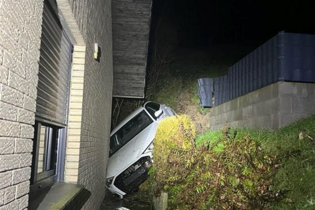 Ein Auto steckt zwischen einem Abhang und einem verklinkerten Wohnhaus fest.