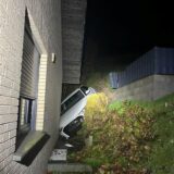 Ein Auto steckt zwischen einem Abhang und einem verklinkerten Wohnhaus fest. 