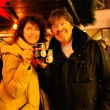 Eine lockige Frau und ein Mann mit Brille stoßen auf dem Dortmunder Weihnachtsmarkt mit der Pinguin-Tasse an.
