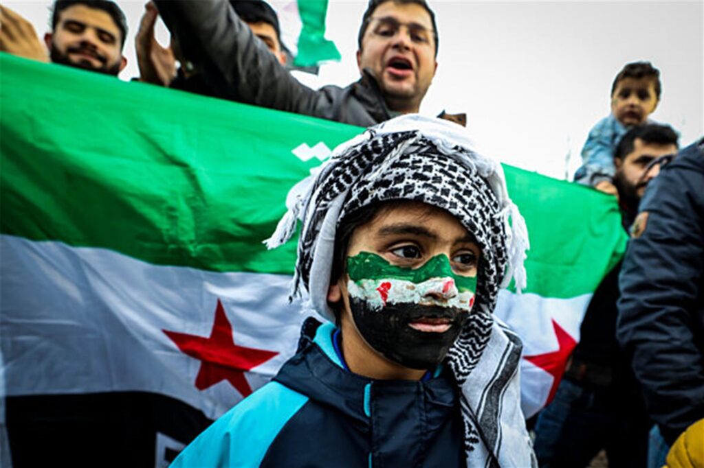 Ein kleiner Junge mit der syrischen Landesfahne ins Gesicht gemalt und einem Palästinensertuch um den Kopf. Menschen feiern den Sturz des Assad-Regimes in Syrien. Ein kleiner Junge mit der syrischen Landesfahne ins Gesicht gemalt und einem Palästinensertuch um den Kopf. Menschen feiern den Sturz des Assad-Regimes in Syrien.