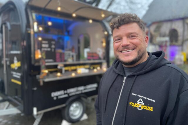Ein Bild von Deniz Mert, direkt vor seinem „Toast House“ in Werne am Markt. Er lächelt in die Kamera.