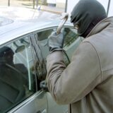 Ein vermummter Dieb versucht mit einem Brecheisen ein Auto aufzubrechen (gestellte Szene)