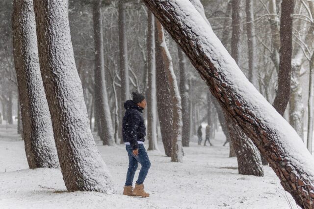 Ein junger Mann geht zwischen Bäumen spazieren, während es schneit.