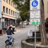 Ein Radfahrer fährt in Unnas Fußgängerzone hinein. In der Bildmontage sind Uhrzeiten auf einem Verkehrsschild grün übermalt.