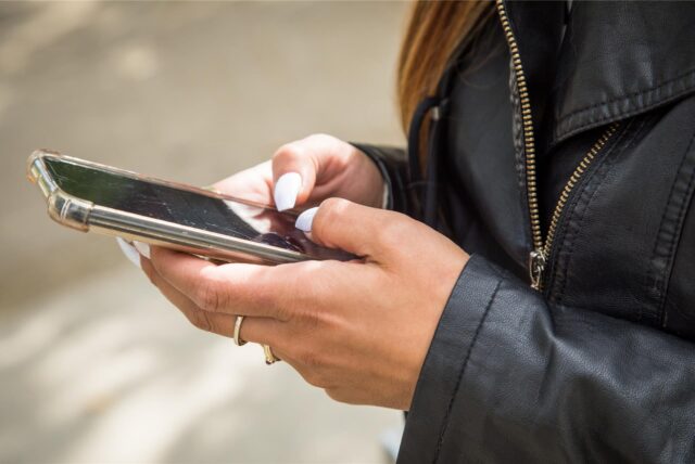Eine Frau mit langen weißen Fingernägeln hält ein Smartphone in der Hand und schreibt eine Nachricht.