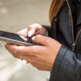 Eine Frau mit langen weißen Fingernägeln hält ein Smartphone in der Hand und schreibt eine Nachricht.