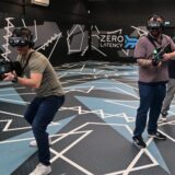 Drei Spieler mit VR-Brillen und Spielzeuggewehren stehen auf einer leeren Spielfläche von Zero Latency.