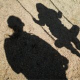 Der Schatten von einem Mann und einem schaukelnden Kind fallen auf Sand auf einem Spielplatz in Braunschweig. (Archivbild)