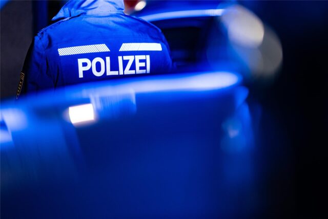 Die Jacke eines Polizisten wird von hinten gezeigt. Es ist deutlich die Aufschrift der Polizei zu erkennen und das Bild ist in einem bläulichen Ton.