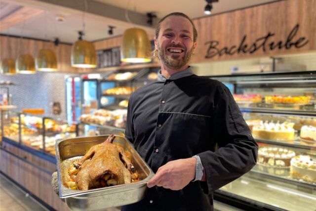 Marcel Appel lacht in die Kamera. Er steht im Verkaufsraum des Cafés. In seinen Händen hält er einen Gänsebraten.