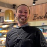 Marcel Appel lacht in die Kamera. Er steht im Verkaufsraum des Cafés. In seinen Händen hält er einen Gänsebraten.