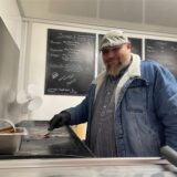 Denis Schäfer brät Burger und lächelt in die Kamera.