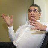 Rudi Assauer sitzt in einem Stuhl und hält in der rechten Hand eine Zigarre zwischen den Fingern.