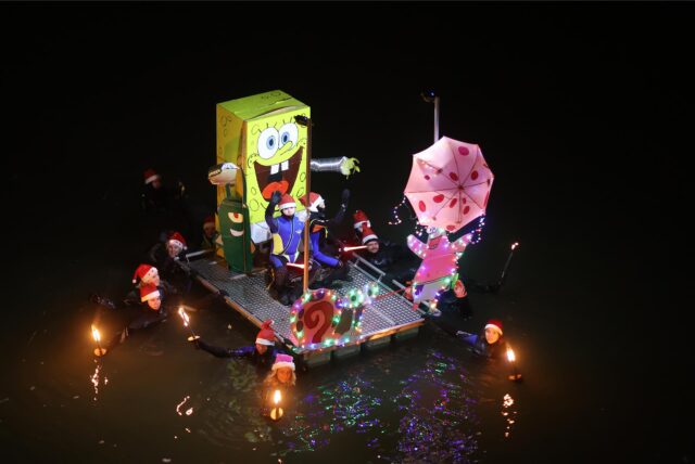 Menschen mit leuchtenden Flößen im Dunkeln im Wasser.