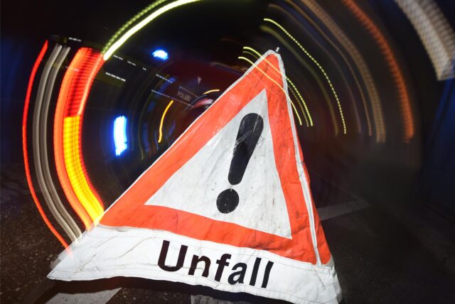 Ein Warndreieck mit dem Schriftzug „Unfall“ steht am 22.06.2015 in Freiburg (Baden-Württemberg) vor einem Blaulicht auf der Straße.