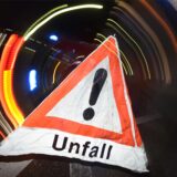 Ein Warndreieck mit dem Schriftzug „Unfall“ steht am 22.06.2015 in Freiburg (Baden-Württemberg) vor einem Blaulicht auf der Straße.