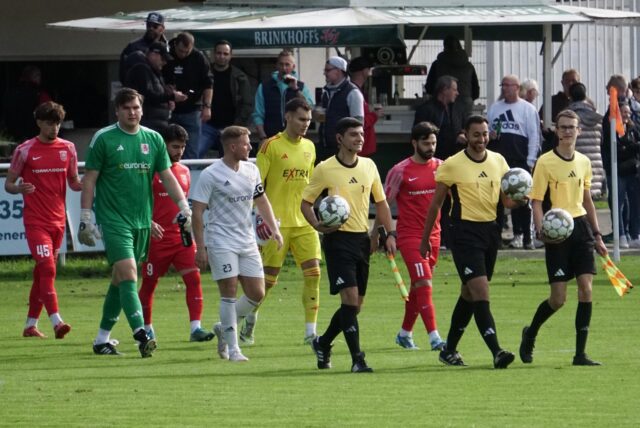 Schiedsrichter führen zwei Fußballmannschaften auf das Feld.