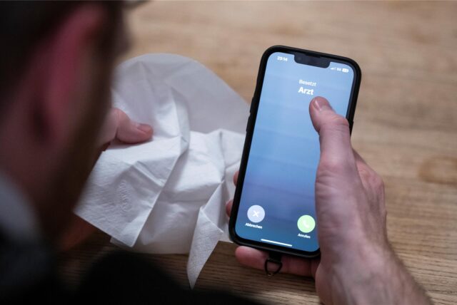 Mann mit Taschentuch und Handy ruft Arzt an.