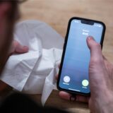 Mann mit Taschentuch und Handy ruft Arzt an.