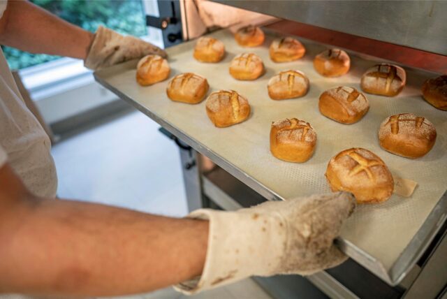 Ein Mann nimmt ein Blech mit Brötchen aus einem Ofen.
