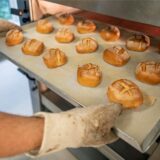 Ein Mann nimmt ein Blech mit Brötchen aus einem Ofen.