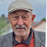 Klaus Holzer (links), rechts eine Frau in weißem Gewand in einem Fluss, von hinten fotografiert.