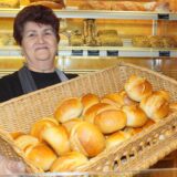 Eine Bäckereifachverkäuferin der Bäckerei Braune in Bergkamen hält eine Kiste mit Brötchen in die Kamera. Sie lächelt.
