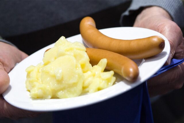 Würstchen mit Kartoffelsalat liegen auf einem Teller.