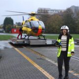 Vor einem gelben Hubschrauber stehen zwei Menschen und reden. Eine Person hält ein Mikrofon.