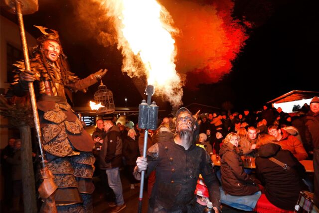 Ein Feuerspucker bei Nacht. Drumherum viele Menschen, die ihm zuschauen.