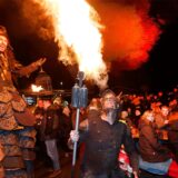 Ein Feuerspucker bei Nacht. Drumherum viele Menschen, die ihm zuschauen.