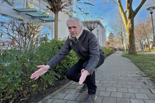 Anwohner Thomas Averbeck hockt an der Bertha-von-Suttner-Allee in Unna und zeigt mit ausgebreiteten Händen einen Abstand an.