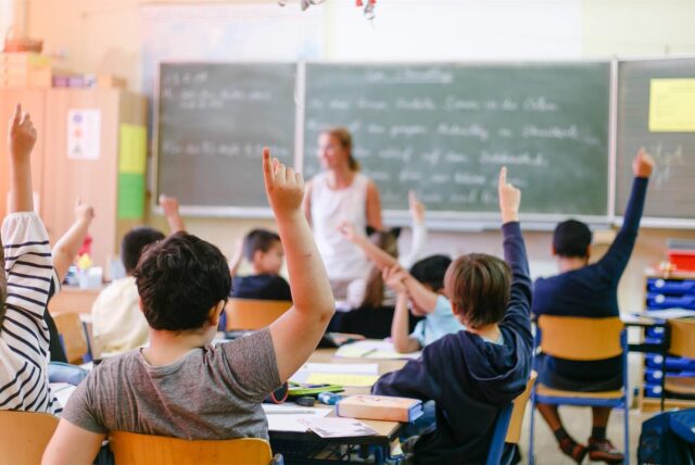 Schulinder zeigen im Klassenraum auf.