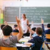 Schulinder zeigen im Klassenraum auf.